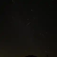 A streak of light is visible against a starry sky over mountains.