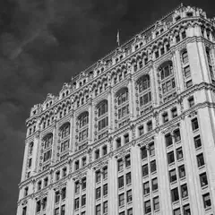 A tall, ornate building with numerous windows and intricate architectural details rises against a dark, cloudy sky.