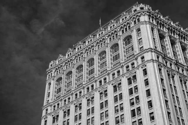 A tall, ornate building with numerous windows and intricate architectural details rises against a dark, cloudy sky.