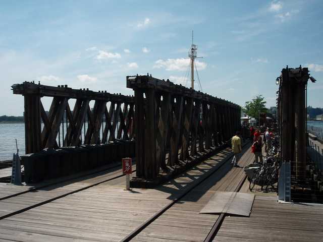 A wooden pier extends toward the water, and a ship's mast is visible in the distance.