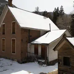 A two-story brick building with a connecting wooden structure stands in snow-covered terrain.
