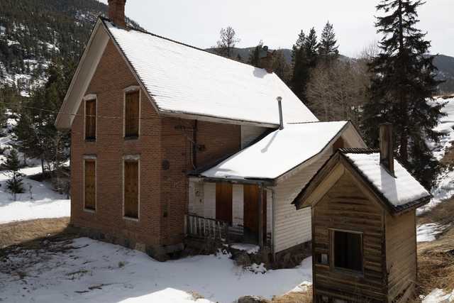 A two-story brick building with a connecting wooden structure stands in snow-covered terrain.