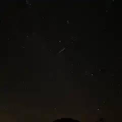 A streak of light is visible against a starry sky over mountains.