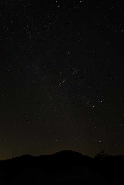 A streak of light is visible against a starry sky over mountains.