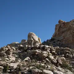 A rock formation rises from a hillside covered in smaller rocks and sparse vegetation.