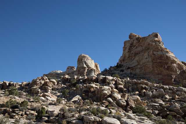 A rock formation rises from a hillside covered in smaller rocks and sparse vegetation.