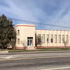 A beige building with red accents and large windows sits on a street corner.