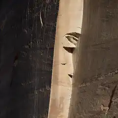 The image shows a large, eroded rock face carved into a cliff side, illuminated by sunlight.