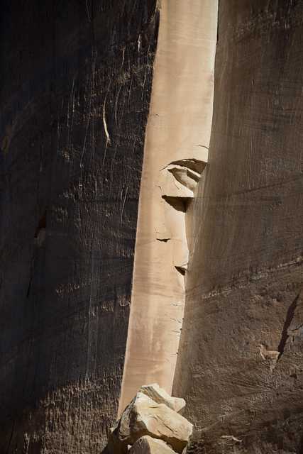 The image shows a large, eroded rock face carved into a cliff side, illuminated by sunlight.
