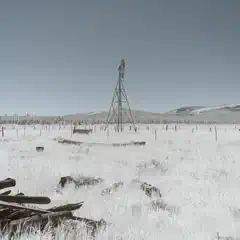 A windmill stands in a dry, grassy field with scattered wooden debris in the foreground.