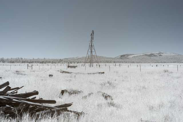 A windmill stands in a dry, grassy field with scattered wooden debris in the foreground.