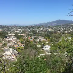 A residential area extends toward distant, tree-covered mountains under a clear blue sky.