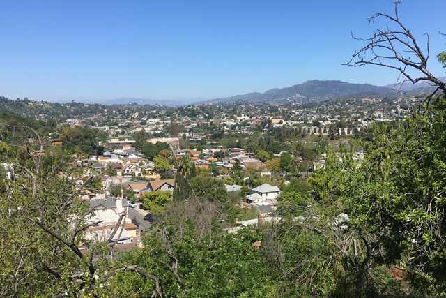 A residential area extends toward distant, tree-covered mountains under a clear blue sky.