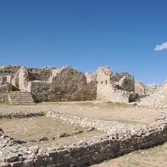A large ruin of stone walls and foundations under a clear blue sky.