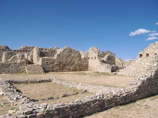 A large ruin of stone walls and foundations under a clear blue sky.