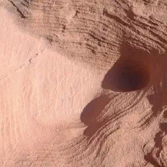 A red rock formation with a dark hole and smooth, wavy lines on its surface.