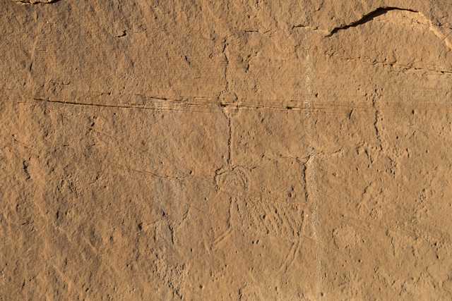 A sandstone wall incorporates petroglyphs including linear designs and a humanlike form.