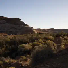 A narrow canyon contains scrub brush and dirt ground, with rock walls rising on either side.