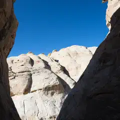 A narrow canyon frames a distant, light-colored rock formation under a blue sky.