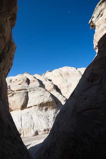 A narrow canyon frames a distant, light-colored rock formation under a blue sky.