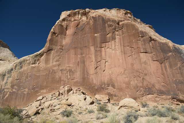 A large rock formation with red and brown hues, featuring a flat top and jagged edges, set against a clear blue sky.