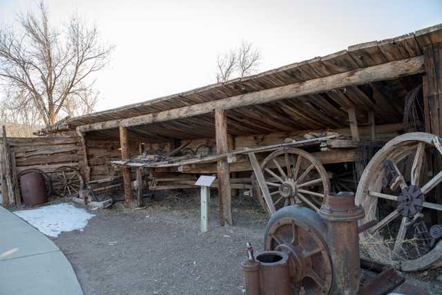 An old wooden shed with a sloping roof is filled with various pieces of rusted machinery and equipment, including large wheels and metal parts.