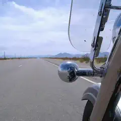 A highway stretches into a distant, mountainous landscape, partially framed by a motorcycle's bodywork.