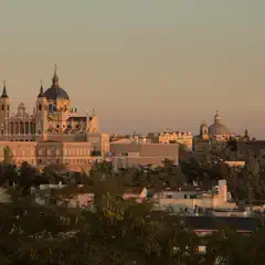 A cityscape at sunset, featuring historic buildings with domes and towers, set against a hazy sky.
