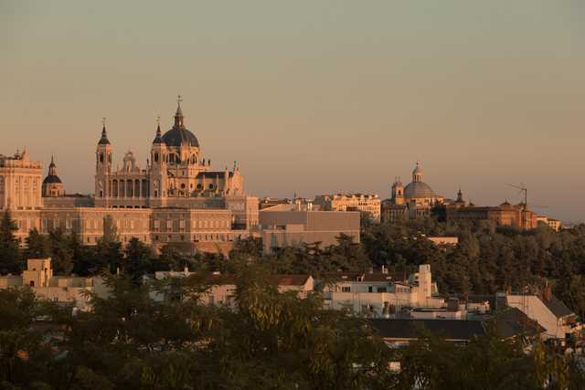 A cityscape at sunset, featuring historic buildings with domes and towers, set against a hazy sky.