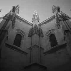 A gothic building features detailed stonework, narrow windows, and pointed spires extending upward from the walls.