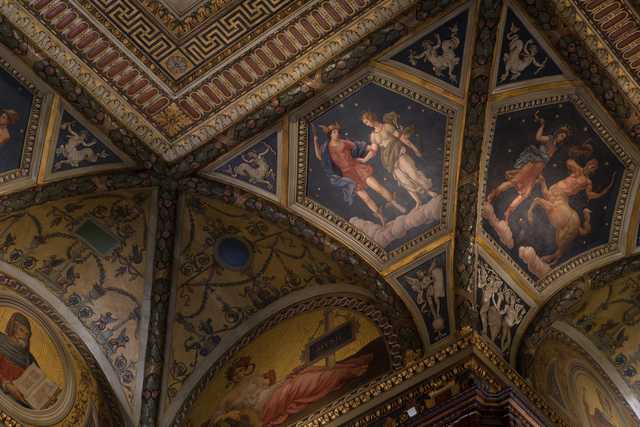 Ceiling featuring intricate gilded moldings, frescoed panels of mythological figures, and geometric patterns framed by ornate arches.