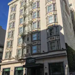 A beige building with ornate details and windows is situated on the corner of a street, featuring a fire escape staircase in the middle.