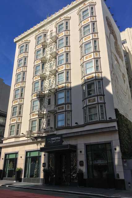 A beige building with ornate details and windows is situated on the corner of a street, featuring a fire escape staircase in the middle.