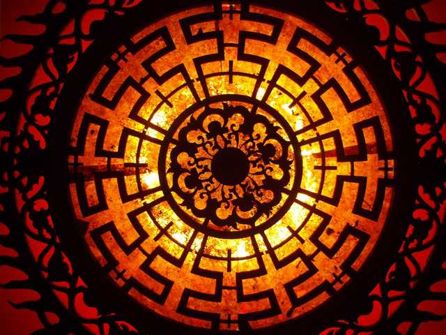 A circular design features a central black floral element surrounded by a labyrinthine pattern in shades of orange and yellow.