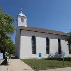 A white church with a steeple and stained glass windows under clear blue skies.