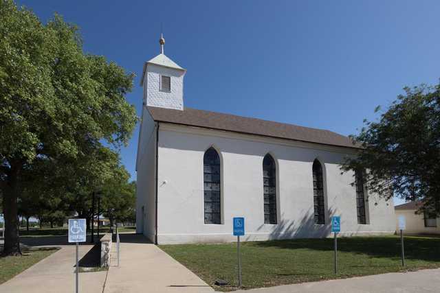 A white church with a steeple and stained glass windows under clear blue skies.