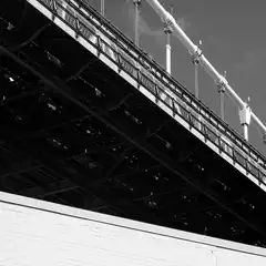 A bridge's intricate steel framework and ornate railing are captured from below, with a brick building in the foreground.