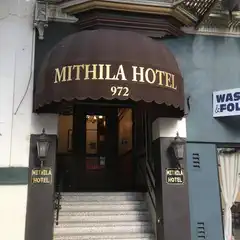 A brown awning with gold lettering marks the entrance to a hotel, situated above a set of stairs leading up to the building's main door.