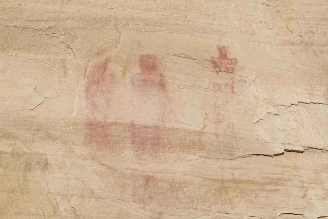 Three human figures painted in red on a rocky surface.