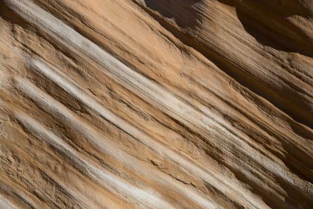 A rock face displays diagonal bands of brown and white sediment.