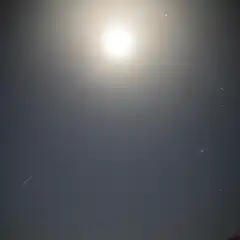 A bright moon dominates a dark sky with scattered stars and a dark, rolling hill in the foreground.