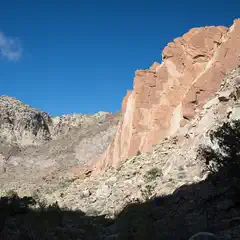 A large red rock formation rises from a desert landscape under a clear blue sky.