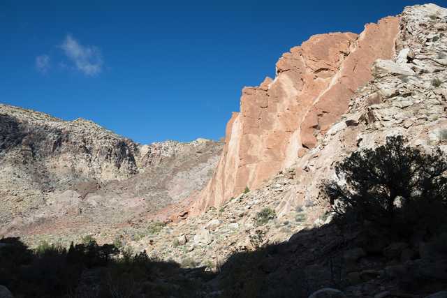 A large red rock formation rises from a desert landscape under a clear blue sky.