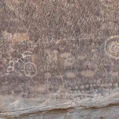 A large rock formation features ancient petroglyphs, showcasing various animals and circular symbols etched into its surface.
