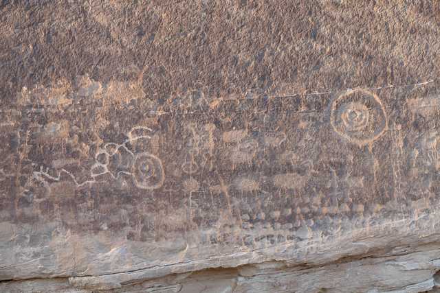 A large rock formation features ancient petroglyphs, showcasing various animals and circular symbols etched into its surface.