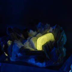 A glowing yellow crystal is nestled among dark blue crystals on a blue base.