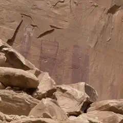 Faded red pictographs of human-like figures are visible on a weathered sandstone wall above a pile of large, angular boulders.