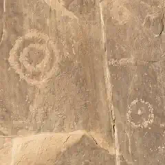 A reddish-brown rock face features two circular petroglyphs embedded in its surface.