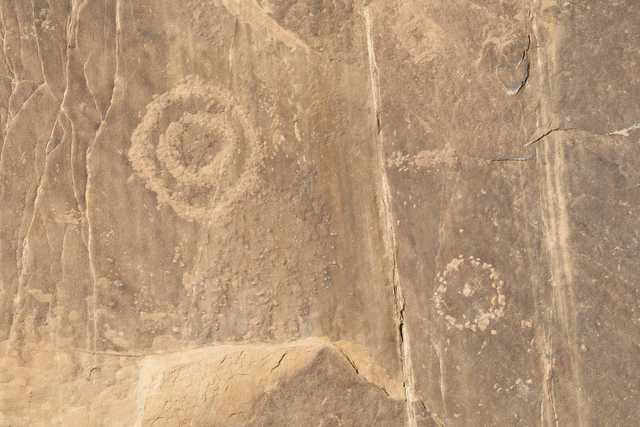 A reddish-brown rock face features two circular petroglyphs embedded in its surface.