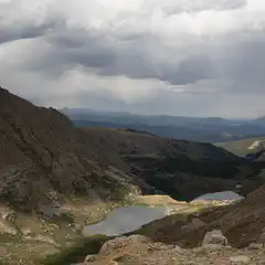 A valley contains two lakes, flanked by steep, rocky slopes under a cloudy sky.